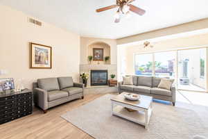 Living room with a ceiling fan, a fireplace, light wood-type flooring, and a textured ceiling