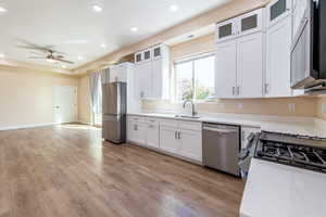 Kitchen featuring glass insert cabinets, stainless steel appliances, white cabinetry, light wood-style floors, and recessed lighting