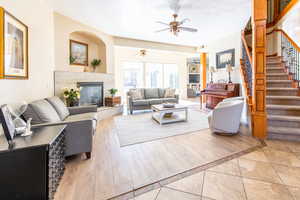 Living room with a tiled fireplace, a textured ceiling, light wood finished floors, and ceiling fan