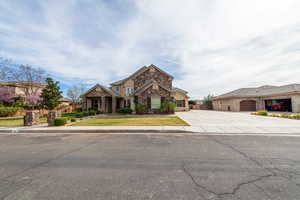 View of front of house with stone siding, driveway, a garage, and a front lawn