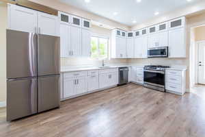Kitchen featuring stainless steel appliances, glass insert cabinets, white cabinetry, light wood-style flooring, and recessed lighting