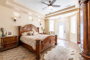 Bedroom featuring a raised ceiling, light wood-style flooring, ceiling fan, access to outside, and a textured ceiling