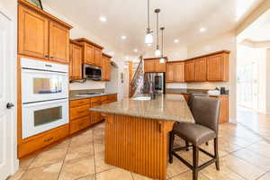 Kitchen with dark stone countertops, stainless steel appliances, wood finish cabinetry, a kitchen island with sink, and a breakfast bar