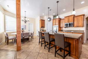 Kitchen with wood finish cabinets, suspended lighting, dark stone counters, stainless steel appliances, and an island with sink