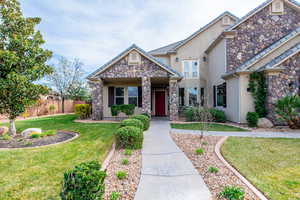 View of front of home featuring stucco siding, stone siding, and a balcony