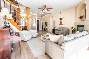 Living area with a textured ceiling, a high end fireplace, a ceiling fan, light wood-style flooring, and arched walkways