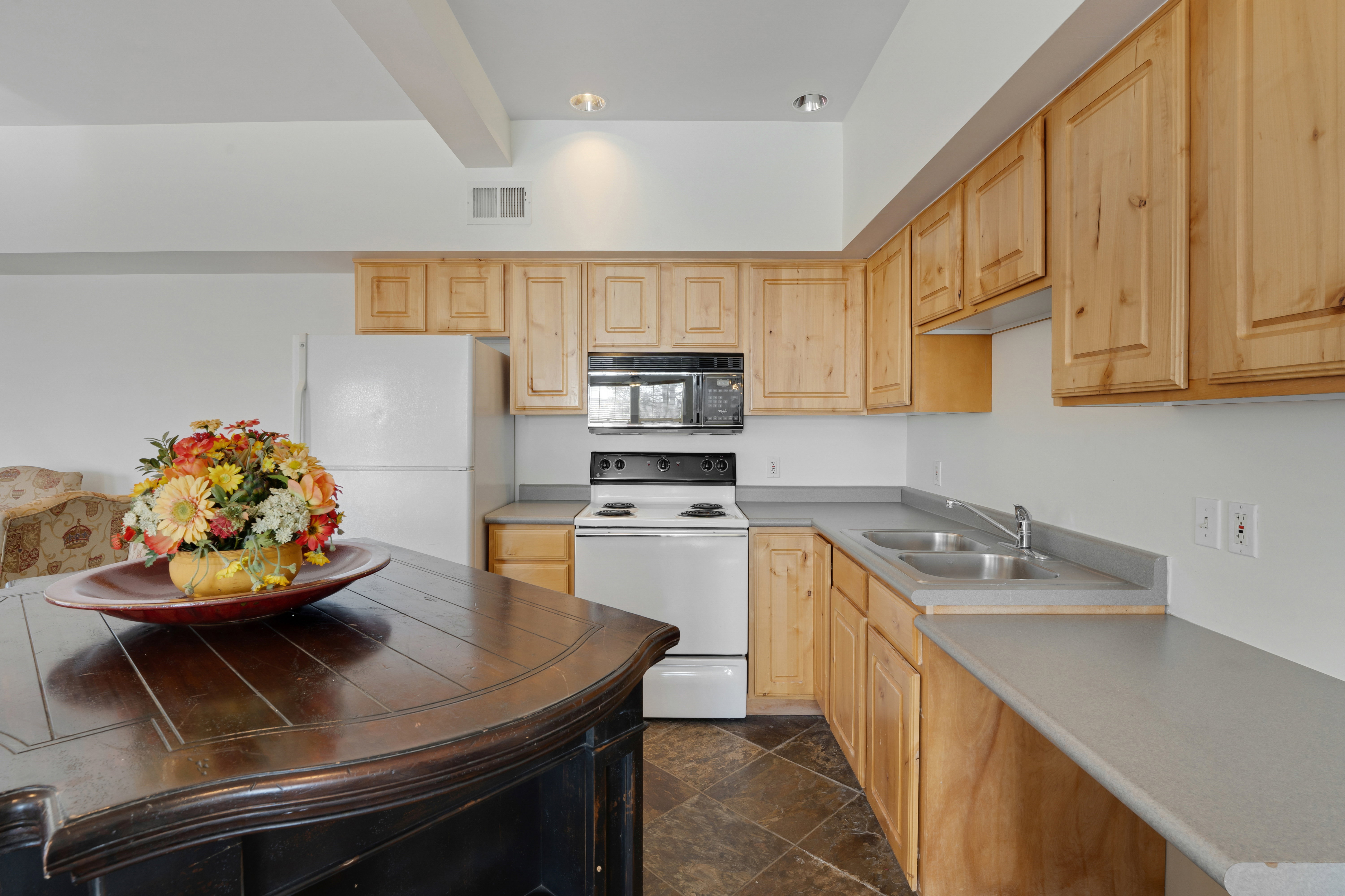 Kitchen featuring white appliances, light wood finish cabinets, dark stone finish floors, beam ceiling, and light countertops