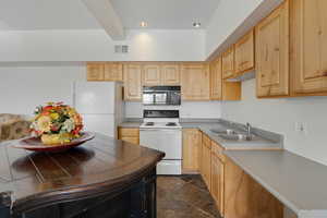 Kitchen featuring white appliances, light wood finish cabinets, dark stone finish floors, beam ceiling, and light countertops