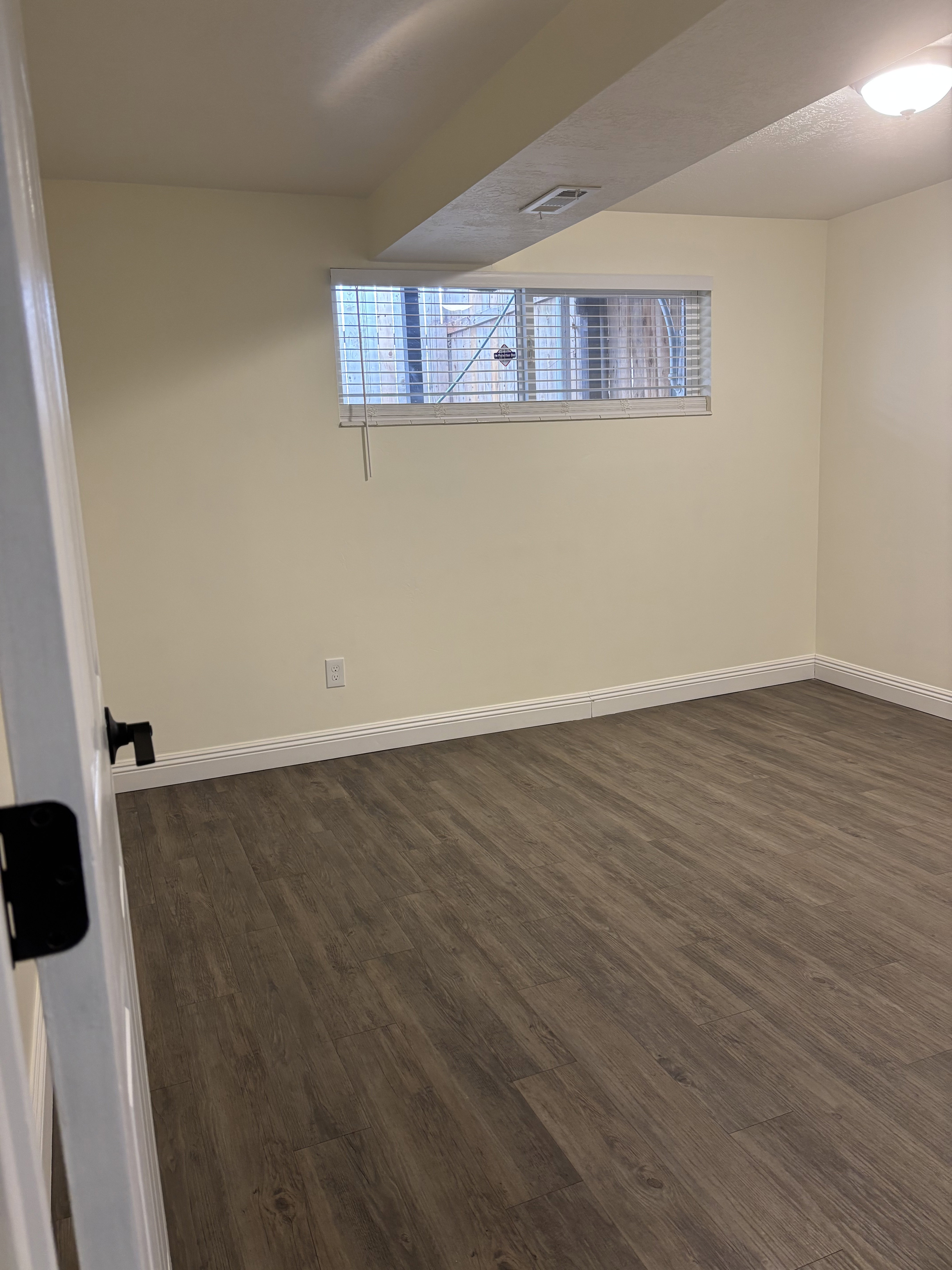 Room featuring wood-finish flooring, light-toned walls, and a recessed window with blinds