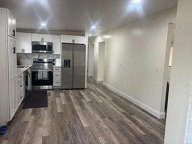 Kitchen featuring light countertops, stainless steel appliances, white cabinetry, dark wood-style flooring, and decorative backsplash