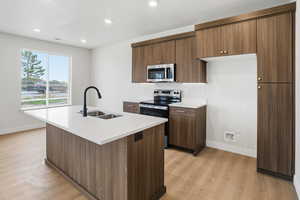 Kitchen featuring stainless steel appliances, light wood-type flooring, a kitchen island with sink, recessed lighting, and modern cabinets