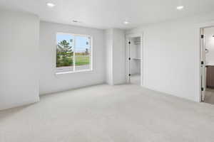 Unfurnished bedroom with light colored carpet, recessed lighting, and a walk in closet