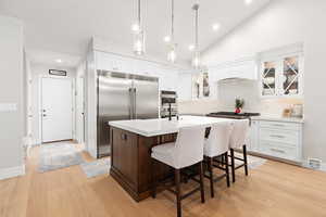 Kitchen with a kitchen bar, stainless steel appliances, an island with sink, glass fronted cabinets, and hanging light fixtures