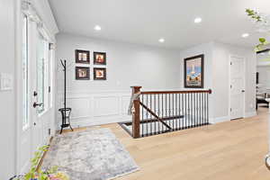 Corridor featuring an upstairs landing, light wood finished floors, recessed lighting, a decorative wall, and wainscoting