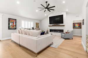 Living room with light wood-type flooring, a ceiling fan, a stone fireplace, and recessed lighting