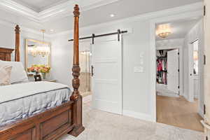 Bedroom with a barn door, light carpet, recessed lighting, ornamental molding, and ensuite bathroom