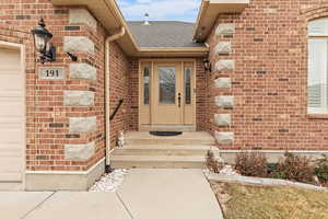 View of exterior entry with brick siding and a shingled roof