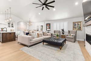 Living area with vaulted ceiling, light wood-style floors, hanging lights, a ceiling fan, and a stone fireplace