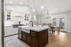 Kitchen with lofted ceiling, an island with sink, dual tone cabinetry, glass insert cabinets, and stainless steel appliances