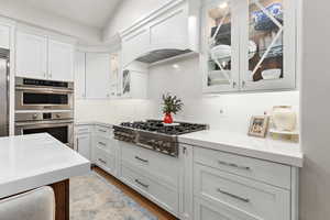 Kitchen with white cabinetry, glass insert cabinets, stainless steel appliances, and wood finished floors