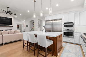 Dual tone kitchen featuring stainless steel appliances, a breakfast bar, open floor plan, a kitchen island with sink, and light wood-style flooring