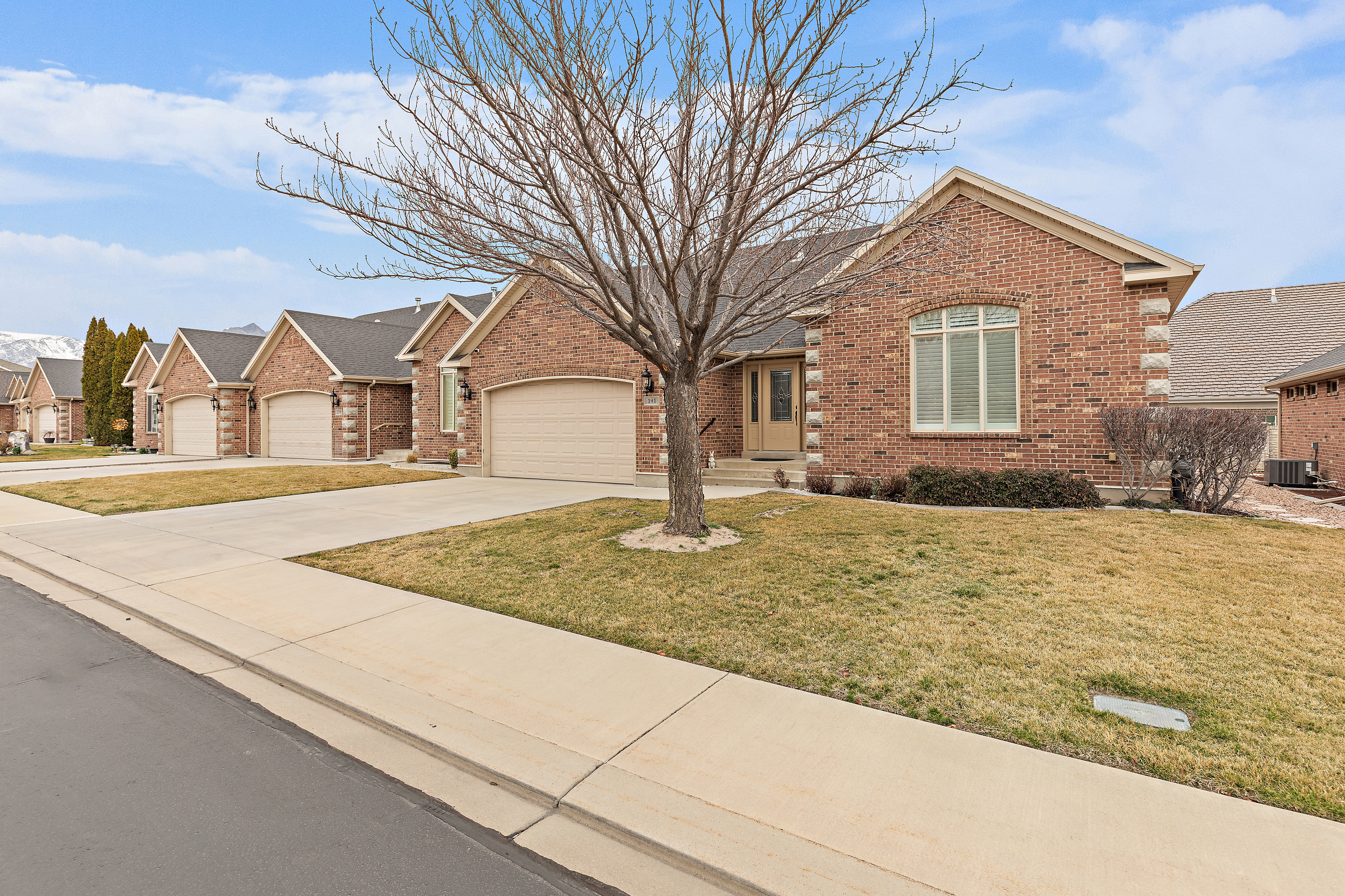 View of front of home featuring driveway, a front yard, brick siding, a residential view, and an attached garage