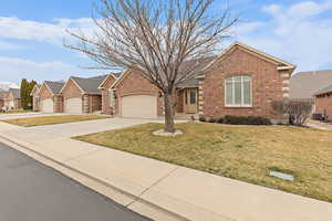 View of front of home featuring driveway, a front yard, brick siding, a residential view, and an attached garage
