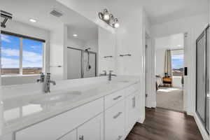 Ensuite bathroom featuring double vanity, a shower stall, and dark wood-style floors