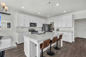 Kitchen with white cabinets, stainless steel appliances, a kitchen breakfast bar, dark wood-style flooring, and recessed lighting