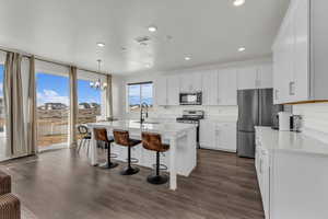 Kitchen with stainless steel appliances, white cabinets, an island with sink, a kitchen breakfast bar, and dark wood-style flooring