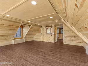 Additional living space with wooden walls, recessed lighting, dark wood-type flooring, a barn door, and vaulted ceiling