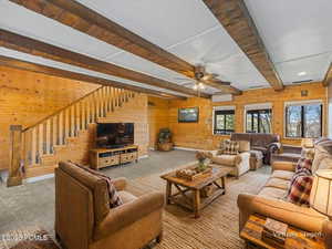 Virtually Staged Living room with wooden walls, beamed ceiling, carpet, and ceiling fan