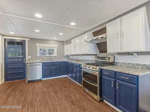 Dual tone kitchen with dual tone cabinets, stainless steel appliances, dark wood-style flooring, light stone counters, and recessed lighting