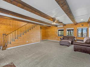 Living area featuring beam ceiling, wooden walls, carpet flooring, and ceiling fan