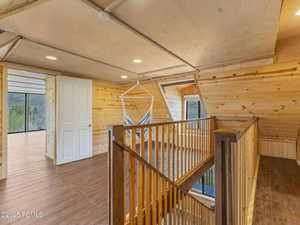 Hall featuring wood walls, an upstairs landing, dark wood-style flooring, recessed lighting, and healthy amount of natural light