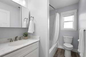 Full bath featuring vanity, shower / tub combo with curtain, and dark wood-type flooring