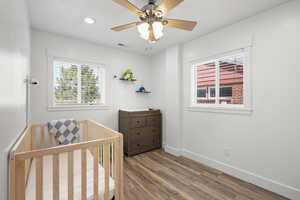 Bedroom with wood finished floors, a ceiling fan, a nursery area, and recessed lighting