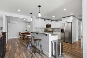 Kitchen with stainless steel appliances, a breakfast bar area, hanging light fixtures, white cabinetry, and a peninsula