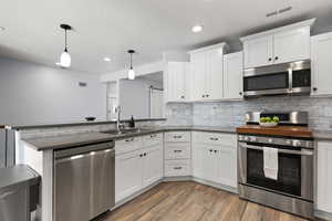 Kitchen with stainless steel appliances, hanging light fixtures, dark wood-type flooring, a peninsula, and white cabinetry