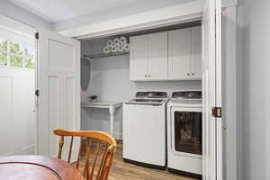 Laundry area with cabinet space, light wood finished floors, and washer and clothes dryer