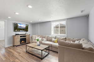 Living area with a textured ceiling, light wood finished floors, a warm lit fireplace, and recessed lighting