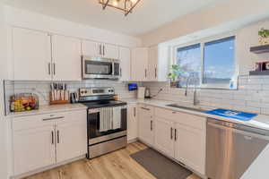 Kitchen featuring stainless steel appliances, white cabinets, light wood finished floors, and light stone counters