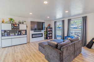 Living area featuring light wood-style floors, recessed lighting, and a glass covered fireplace