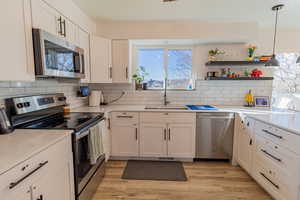Kitchen featuring stainless steel appliances, pendant lighting, white cabinets, light wood-style floors, and backsplash