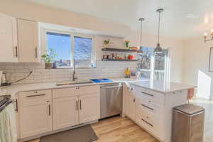 Kitchen featuring a peninsula, stainless steel appliances, white cabinetry, light wood-type flooring, and backsplash