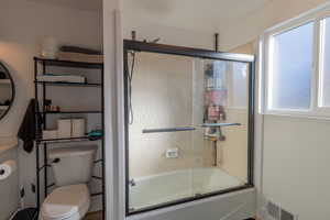 Bathroom featuring toilet and bath / shower combo with glass door