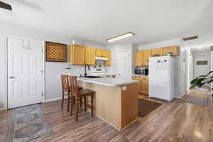 Kitchen featuring white appliances, light countertops, a kitchen breakfast bar, a peninsula, and dark wood finished floors