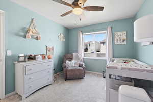 Bedroom featuring light colored carpet, a crib, and ceiling fan