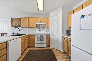 Kitchen featuring white appliances, light countertops, light wood-style flooring, a peninsula, and a textured ceiling