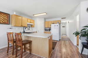 Kitchen with light countertops, white appliances, a peninsula, light wood-style flooring, and light wood finish cabinets